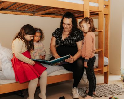 Une personne lit un livre à trois enfants dans une chambre.